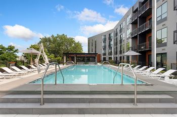 a swimming pool with chaise lounge chairs and umbrellas in front of an apartment building